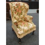 A small wing back easy chair on cabriole legs upholstered in greed  and red floral design on a