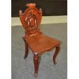 A Victorian carved mahogany hall chair the scroll shield back over a plank seat on cabriole legs,