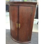 A George III oak and mahogany crossbanded bow front hanging corner cupboard with a shaped interior