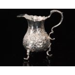 A George II hallmarked silver cream jug raised on three pad feet with later embossed foliate