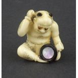 Japanese stained ivory netsuke modelled as a seated oni with drum, mother of pearl inlay, signed