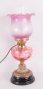 An Antique, now electric Oil Lamp with a cranberry glass shade and a flashed ruby font on a brass