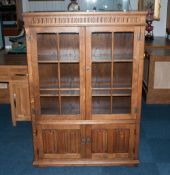 A Golden Oak Double Door Glazed Display Cabinet with the mock jacobean style with 2 linen fold
