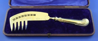 A cased Edwardian silver gilt combination fish slice/fork, with ornate scroll handle and pierced