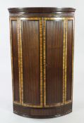 A George III mahogany and rosewood crossbanded reeded hanging corner cupboard, with a pair of