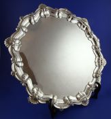 A George V silver salver, of shaped circular form, with a shell and scroll border, on three scroll