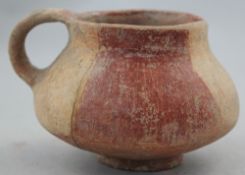 A Greek terracotta cup, c.2nd century BC, of compressed globular form with a looped handle, on a