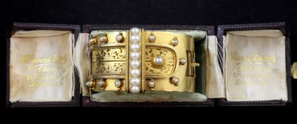 A late Victorian 18ct gold and split pearl hinged bracelet, with pierced foliate scroll