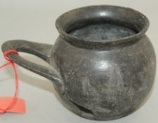 An Etruscan Bucchero ware single handled cup, c. 6th century BC, of globular form with a flat looped