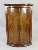 A George III mahogany bowfront hanging corner cupboard, with two doors enclosing shelves, H.3ft