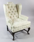 An 18th century style wingback armchair, with scroll arms, upholstered in buttoned cream damask,