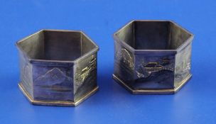A cased pair of Japanese silver hexagonal napkin rings, engraved with seascape and mountainous