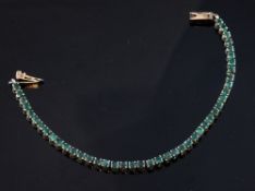 A 14ct gold and emerald line bracelet, set with forty four round cut emeralds, 7in.