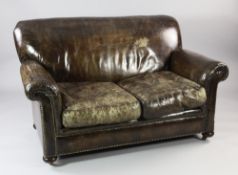 A brass studded brown leather two seat settee, with distressed upholstery with scroll arms and