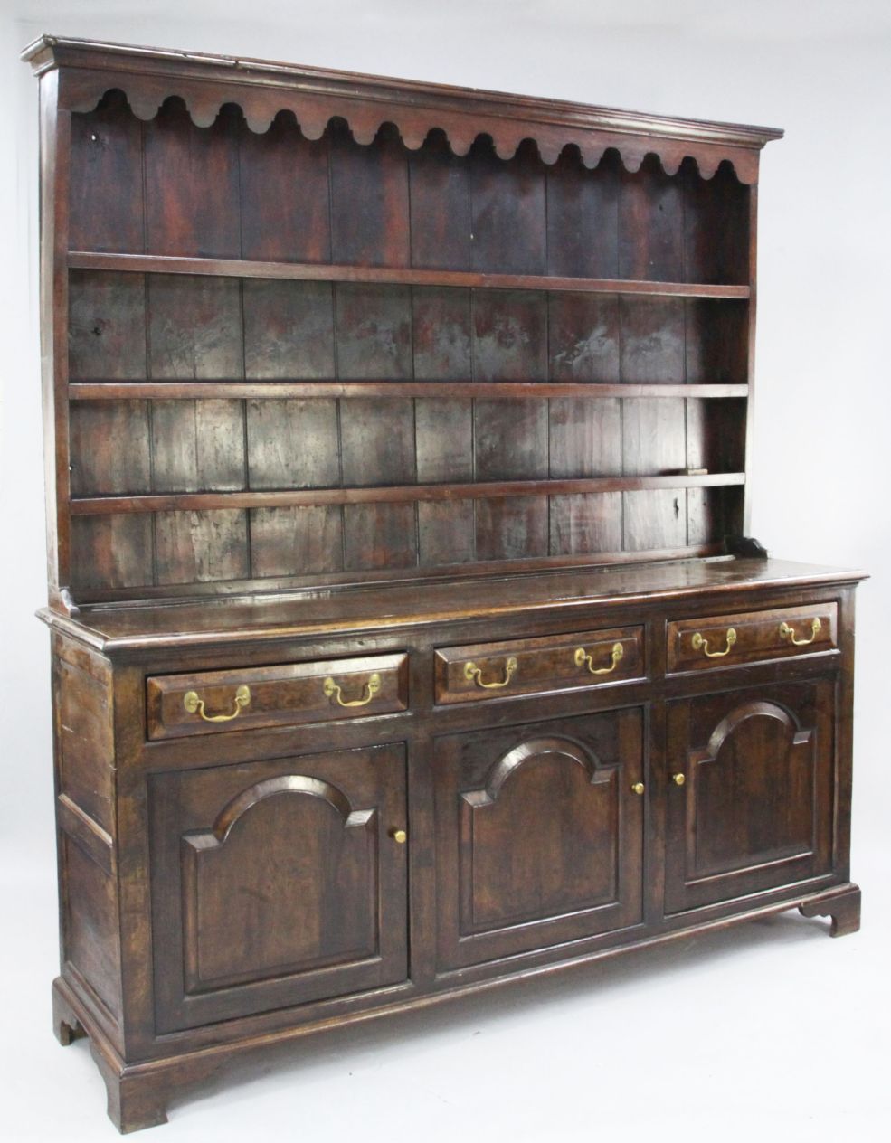 A George III oak dresser, the plate rack with wavy frieze and three fitted shelves, over three
