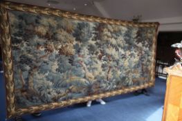 A large Aubusson style tapestry, depicting trees and flowers by a river within an acanthus leaf