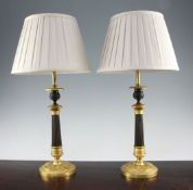 A pair of French Empire style bronze and ormolu table lamps, with circular bases and cream pleated