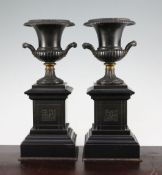 A pair of late 19th century bronze and ormolu campana shaped urns, each on a square pedestal inset