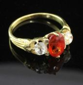 A gold and three stone orange sapphire and diamond ring, set with oval cut sapphire and flanked by