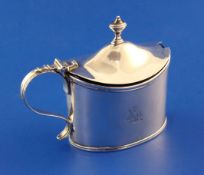 A George III silver mustard pot, of oval form, with engraved armorial, scroll handle and blue