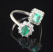 A white gold, emerald and diamond cluster crossover ring, with square and oval shaped clusters, size