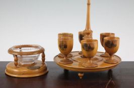 A Mauchlineware egg cruet stand, with six egg cups, on a circular stand, each decorated with various