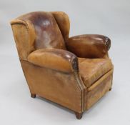 A 1930's brown leather wingback armchair, with brass studded decoration, on shaped feet