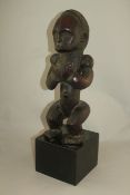 A West African carved hardwood figure of a seated male, with hands clasped to the front, on a square