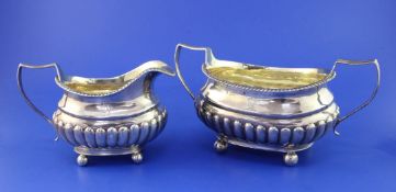 A George III demi-fluted silver oval sugar bowl and cream jug, with engraved armorials, on ball