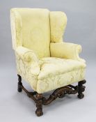 An 18th century style carved walnut wingback armchair, with pale yellow floral pattern damask