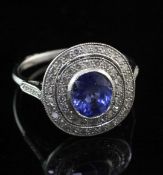 An 18ct white gold, sapphire and diamond cluster target ring, the central oval cut sapphire weighing