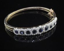 An early 20th century gold, sapphire and diamond hinged bangle, set with nine sapphire and diamond