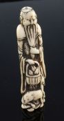 A Japanese stag antler netsuke of a standing sennin, Edo period, holding a basket of peaches with