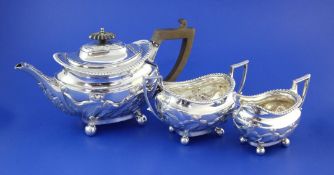 A late Victorian repousse silver three piece tea set, of oval form, with foliate and fluted