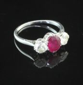 A platinum, ruby and diamond set three stone ring, the central oval cut ruby flanked by two round