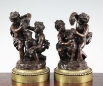 A pair of late 19th / early 20th century patinated bronze putti groups, on circular beaded bases,