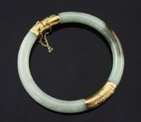 A 14ct gold mounted jadeite hinged bangle, the mounts with engraved decoration.