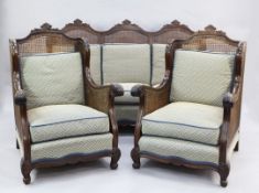 An early 20th century mahogany three piece bergere suite, with double caned sides and acanthus