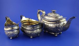 A George III matched silver three piece tea set, of oval form, with later embossed floral