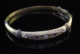 A late Victorian 15ct gold and three stone ruby and diamond set hinged bangle, with cannetile work