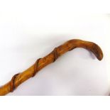 A CARVED WOODEN WALKING STICK with entwined decoration and a brass ferrule, 96cm long.
