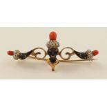 An enamelled Blackamoor brooch  in scrolling yellow metal, further set with coral, bears continental