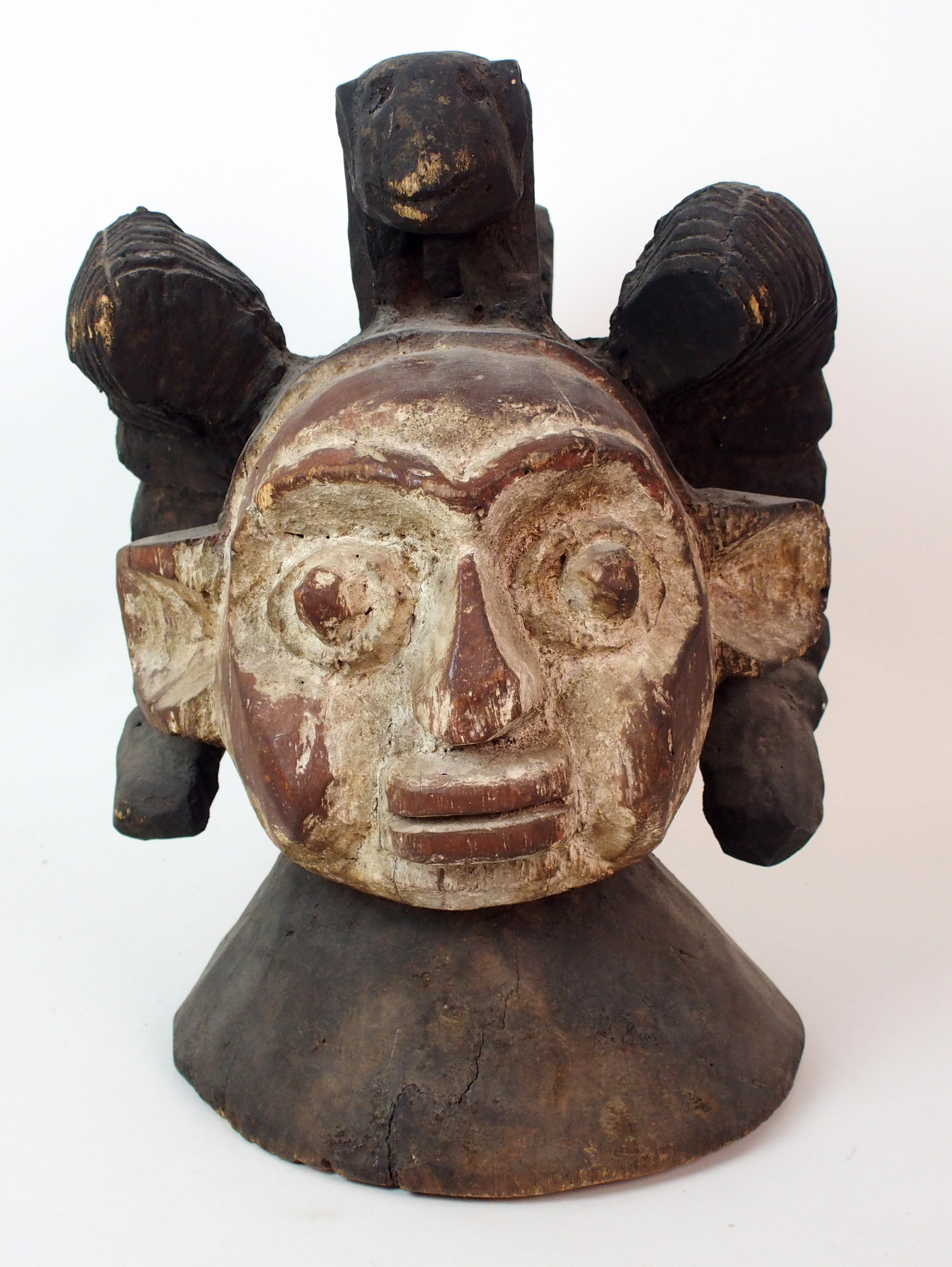 An African carved and painted wood mask with animal finial and scroll shaped ears, 38cm high