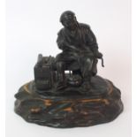 A Japanese bronze of an itinerant worker seated and hollowing out a stem beside a three drawer