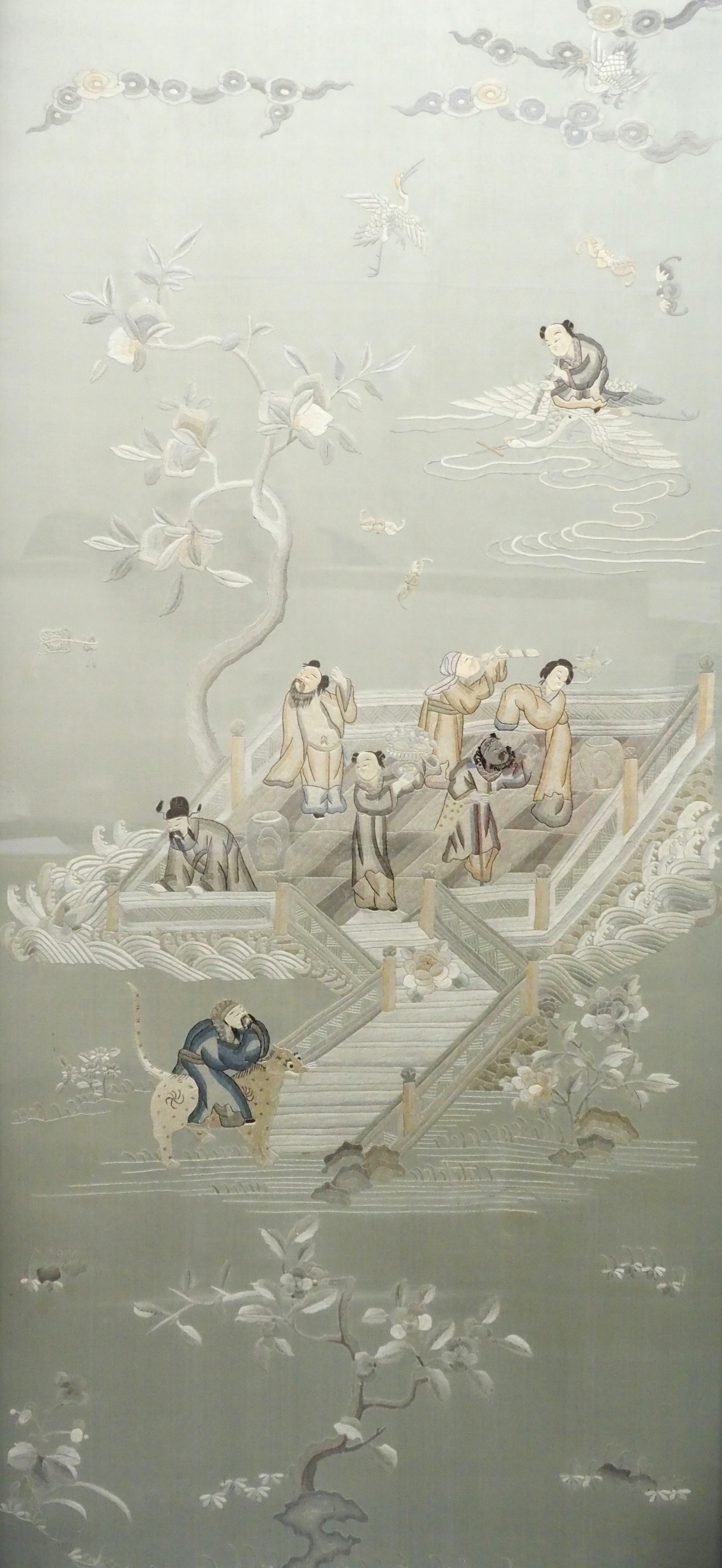 A Chinese silk embroidered picture of figures in a walled garden on an island amongst foliage, 156 x