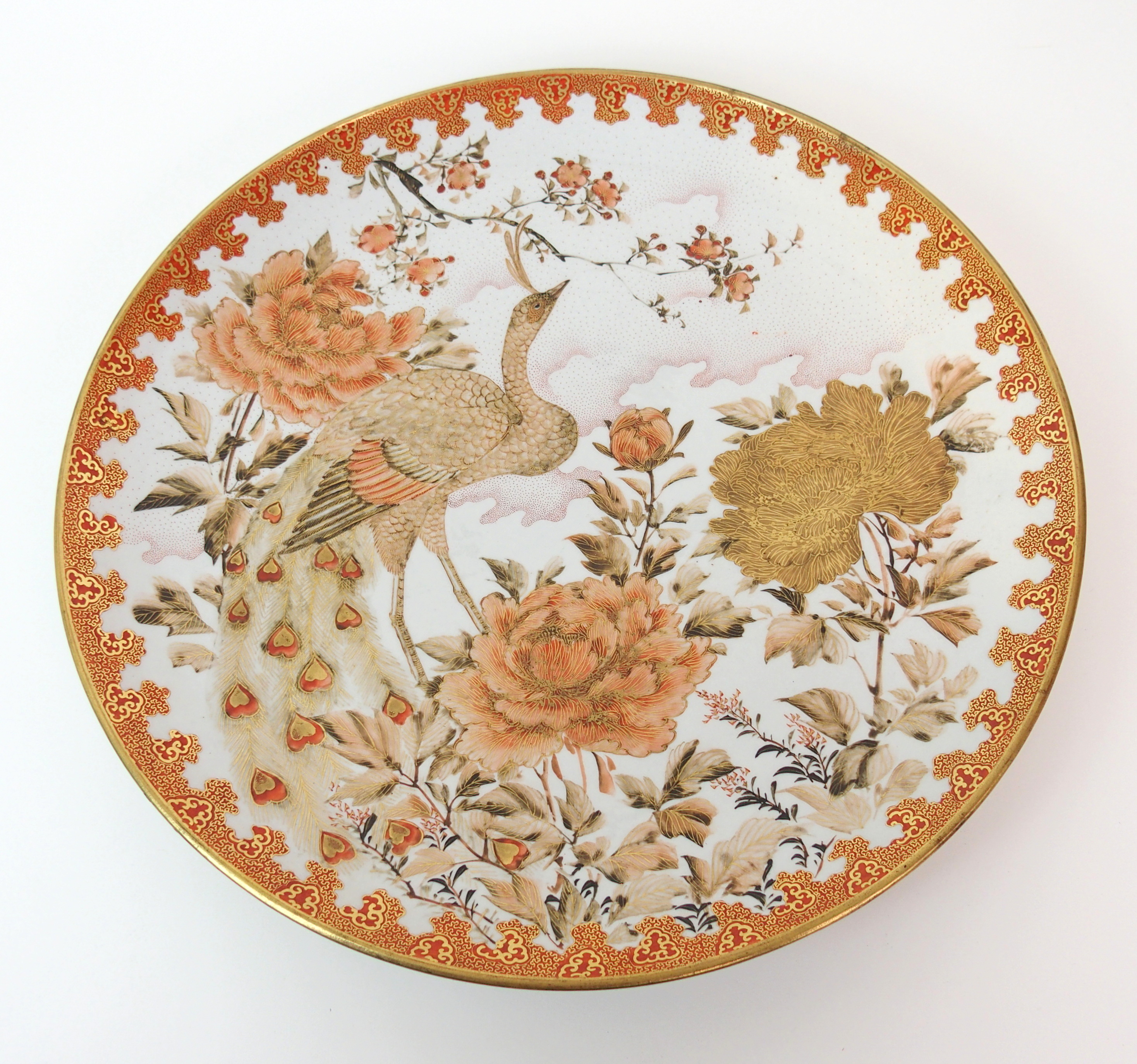 A Kutani dish painted with a peacock amongst peonies and blossoming branches within a red and gilt