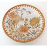 A Kutani dish painted with a peacock amongst peonies and blossoming branches within a red and gilt