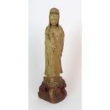 A Chinese soapstone carving of Guanyin standing with a vase clasped to her chest and on a crashing-