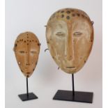 Two African softwood small oval masks each with pierced and indented circles above slit eyes and