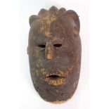 An African stained softwood mask with combed back hair above short ears, pierced eyes and open